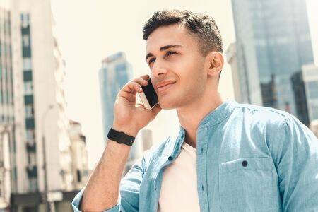 Outdoors Leisure. Stylish guy standing on the street talking on smartphone smiling joyful close-up...