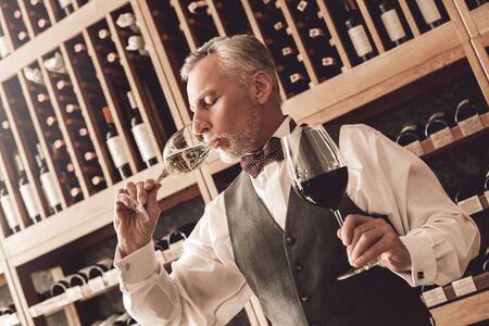 Sommelier Concept. Senior man standing tasting white wine closed eyes concntratedの写真素材