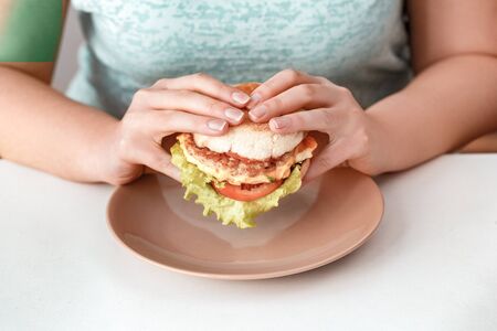 Junk Food. Chubby girl sitting at kitchen eating hamburger plate close-upの写真素材