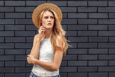 Windy Weather. Young woman in hat standing isolated on wall looking aside concernedの写真素材
