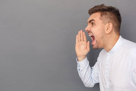 Copy Space for Text or Product. Young man studio standing isolated on grey shouting loud close-up