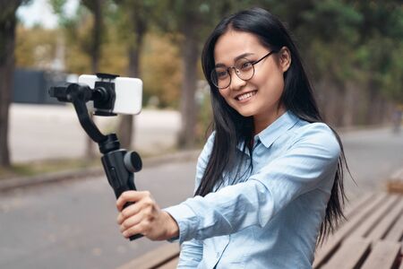 Blogger. Asian girl standing on street with stabilizer taking video on smartphone smiling happyの写真素材