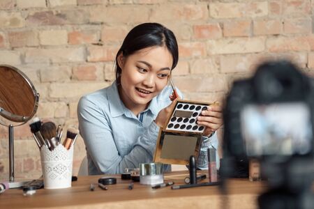 Young adult asian girl making visage and recording video on modern camera