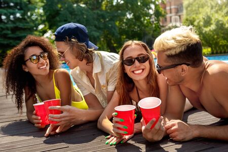 Summer Vacation. Young people in sunglasses lying by the pool holding cocktails talking cheerful