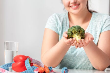 Body Care. Chubby girl sitting at kitchen table holding broccoli close-up smiling cheerfulの写真素材