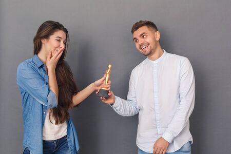 Relationship Concept. Young man smiling happy giving award to woman studio standing isolated on greyの写真素材