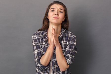 Wish Come True. Young woman standing studio isolated on grey hands in prayer gesture looking camera...