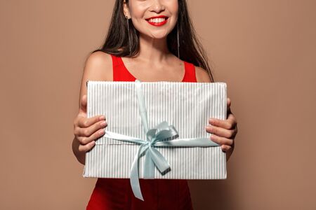Freestyle. Young girl in dress standing isolated on brown with present box close-up smiling happyの写真素材