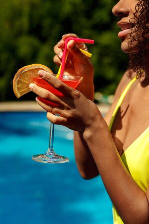 Summer Vacation. Young african woman by the pool drinking cocktail smiling happy close-up