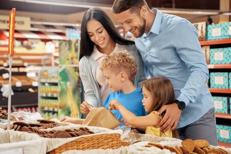 Daily Shopping. Family of four in the supermarket choosing cookies laughing cheerfulの写真素材