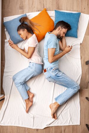Young adult girlfriend and boyfriend lying on bed and using smartphoneの写真素材