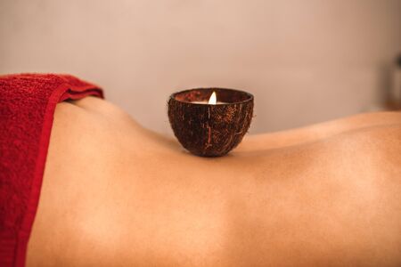 Alternative medicine healing young woman lying bare upper body with aroma candle on her back close-upの写真素材