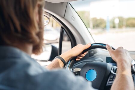 Young man traveling by new electric car transportation sitting inside holding steering wheel driving back view close-upの写真素材