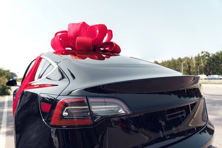Electric black car with ribbon bow luxury present outdoors side view close-upの写真素材