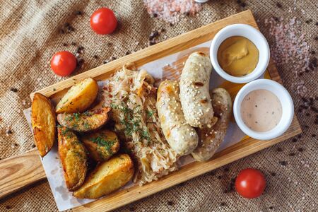 Fresh sausages roasted potatoes with sauces and braised cabbage on wooden board for lunch isolated on table no people top view close-upの写真素材