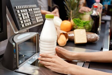 People standing in queue at checkout counter products on conveyor belt while cashier checking out bottle of milk close-upの写真素材