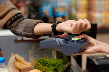 Young woman standing at the supermarket at cashier checkout counter paying for purchases contactless...