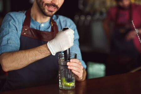 Drink Preparation. Bartender standing at counter squeezing out lime juice pressing hard close-up...