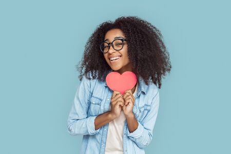 Freestyle. African girl in glasses standing isolated on gray with heart card posing smiling cheerfulの写真素材