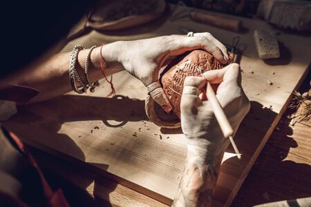 Craftsperson Concept. Young woman making pottery at creative studio creating pattern on cup sitting using modeling tool in the dark top view close-upの写真素材