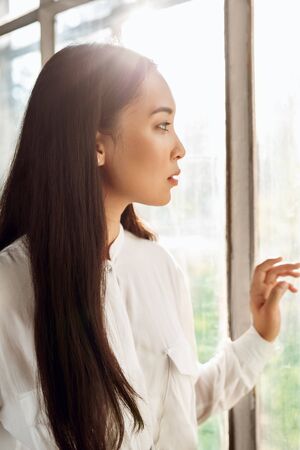 Freestyle. Young woman standing looking out the window at nature curious close-upの写真素材