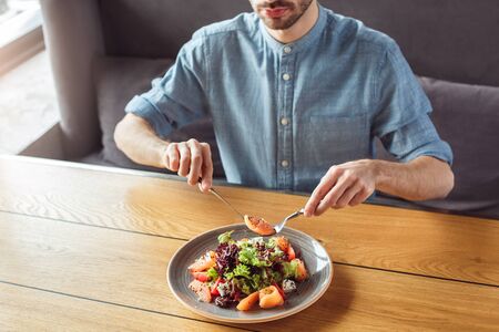 Lunch Time. Guy sitting at table eating salmon salad concentrated close-upの写真素材