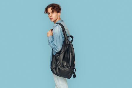 Freestyle. Man in denim shirt with backpack standing isolated on gray looking back curious