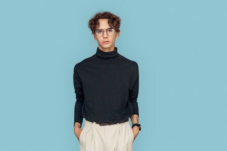 Freestyle. Man in glasses standing isolated on gray hands in pockets posing to camera pensive
