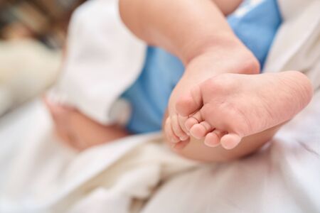 Selective focus on child feet against copy space background. Cropped view of tender and gentle little new born baby lying in bedroom on cozy bedの写真素材