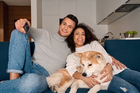 Young adult man, african american woman and dog watching tv at homeの写真素材