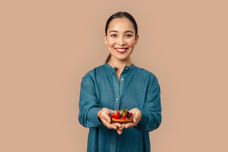 Freestyle. Young woman in denim dress standing isolated on bage giving fruit tart to camera smiling...