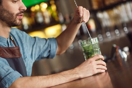 Making Drink. Bartender standing at counter mixing mojito concentrated close-upの写真素材