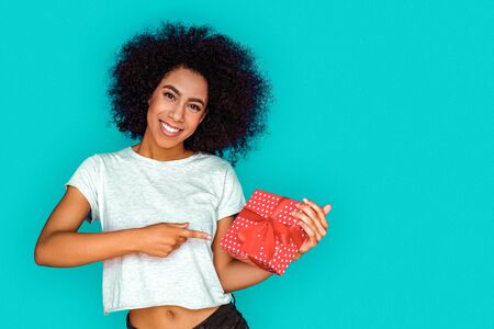 Celebration. Mulatto girl standing isolated on blue pointing at gift smiling cheerfulの写真素材