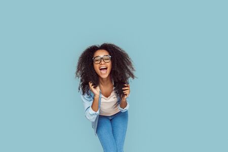 Freestyle. African girl in glasses standing isolated on gray bending forward laughing cheerfulの写真素材
