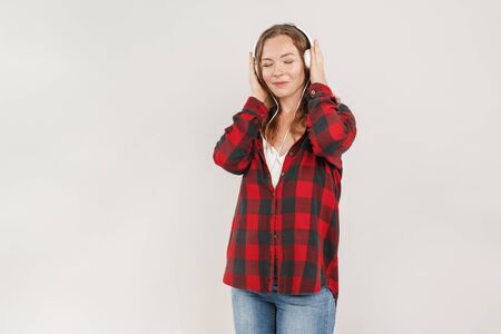 Freestyle. Young woman with freckles wearing headphones standing isolated on grey listening to music closed eyes smiling relaxedの写真素材