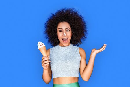 Tasty food. Mulatto girl standing isolated on blue having nose dirty in ice cream smiling playfulの写真素材