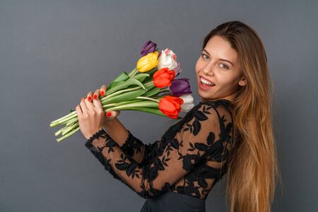 Young woman in black dress studio isolated on gray holding tulips bouquetの写真素材