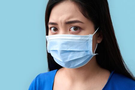 Coronavirus Concept. Chinese woman wearing medical mask standing isolated on grey frightened close-upの写真素材