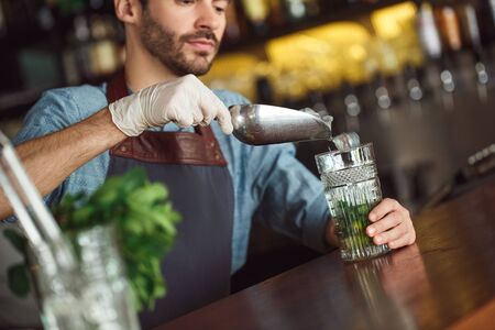 Making Drink. Bartender standing at counter adding ice inro glass concentrated close-upの写真素材