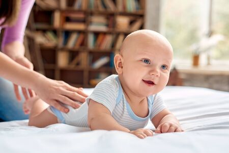 Baby Care. Young mother stroking little son lying on bed on belly holding his head up cheerful close-upの写真素材
