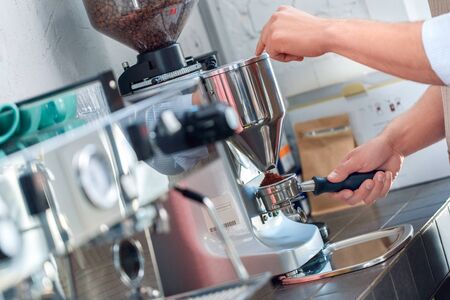 Cropped view of young adult barista working in coffeeshop, standing near professional espresso machine, making freshly ground coffeeの写真素材
