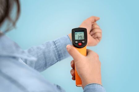 Coronavirus concept. Cropped view of young adult asian girl checking high temperature with infrared...