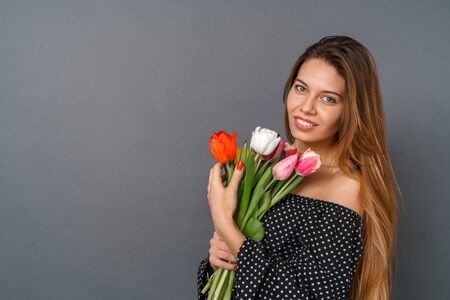 Young woman casual studio isolated on gray with bouquet of tulips looking camera tenderの写真素材