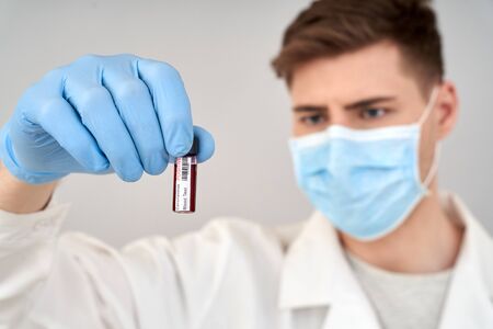 Doctor in robe and medical mask standing isolated on gray with virus in bulb close-up blurred...