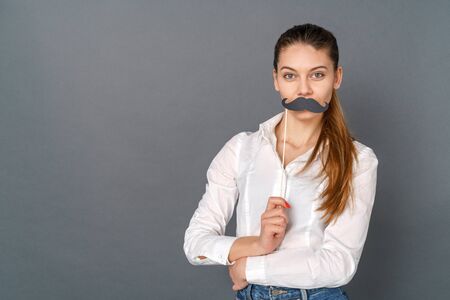 Young woman student studio isolated on gray posing with crafted mustacheの写真素材
