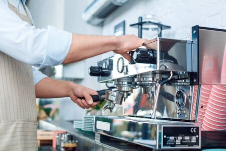 Coffee Passion. Young barista at coffee shop inserting portafilter into coffee machine ready to make espresso shot close-upの写真素材