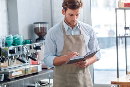 Young adult barista working in cafeteria, making notes in notepadの写真素材