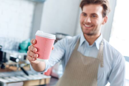 Young adult barista working in coffeeshop, holding paper cup with coffeeの写真素材