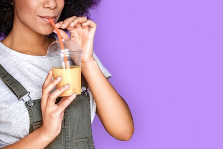 Freestyle. African american girl wearing denim overall standing isolated on blue drinking smoothie joyful close-upの写真素材