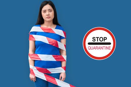 Coronavirus Quarantine. Chinese woman standing isolated on blue covered with warning tape looking camera concerned copy spaceの写真素材